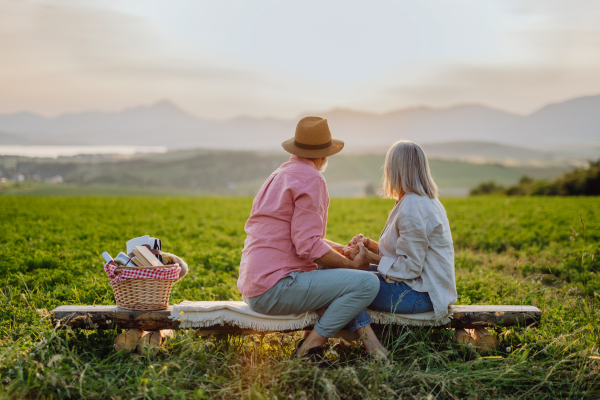 Senior couple sitting at meadow and having romantic moment at the autumn nature. Elderly spouses looking at serene landscape, enjoying beautiful view at High Tatras.