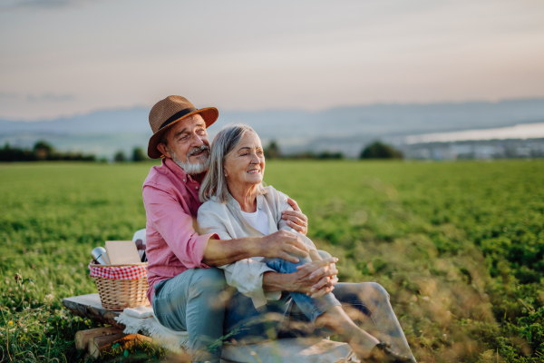 Embracing senior couple watching sunset at the autumn nature, having picnic.