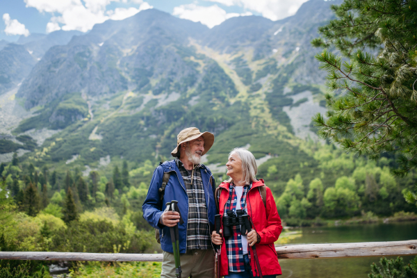 Active elderly couple hiking together in autumn mountains, on senior friendly trail. Senior spouses on the vacation in the mountains celebrating anniversary. Senior tourists with backpacks using trekking poles for stability.