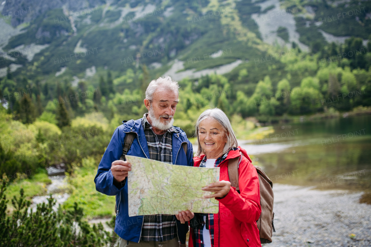 Active elderly couple hiking together in autumn mountains, on senior friendly trail. Senior spouses on the vacation in the mountains celebrating anniversary. Senior tourists with backpacks reading map, preparing for hike.