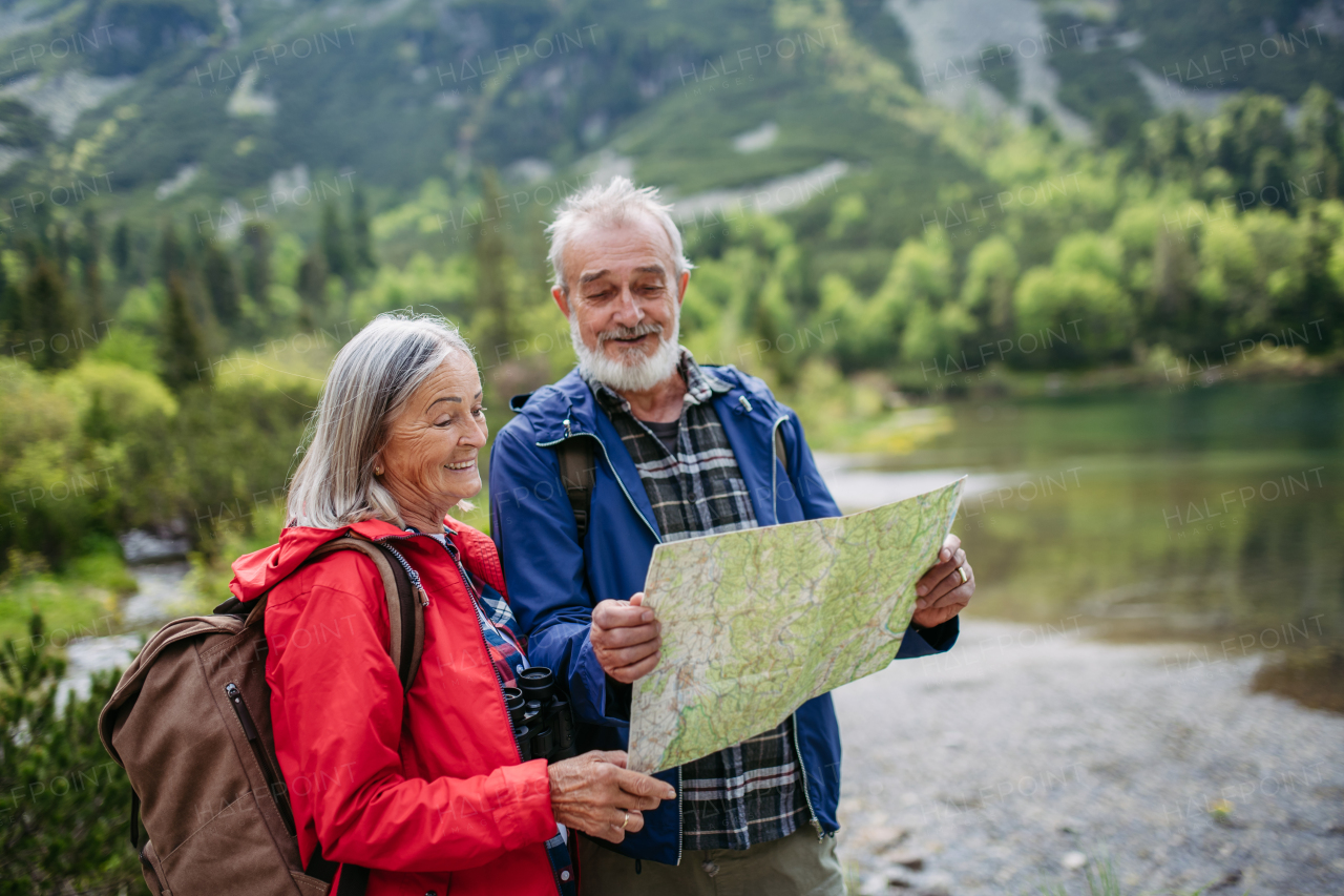 Active elderly couple hiking together in autumn mountains, on senior friendly trail. Senior spouses on the vacation in the mountains celebrating anniversary. Senior tourists with backpacks reading map, preparing for hike.