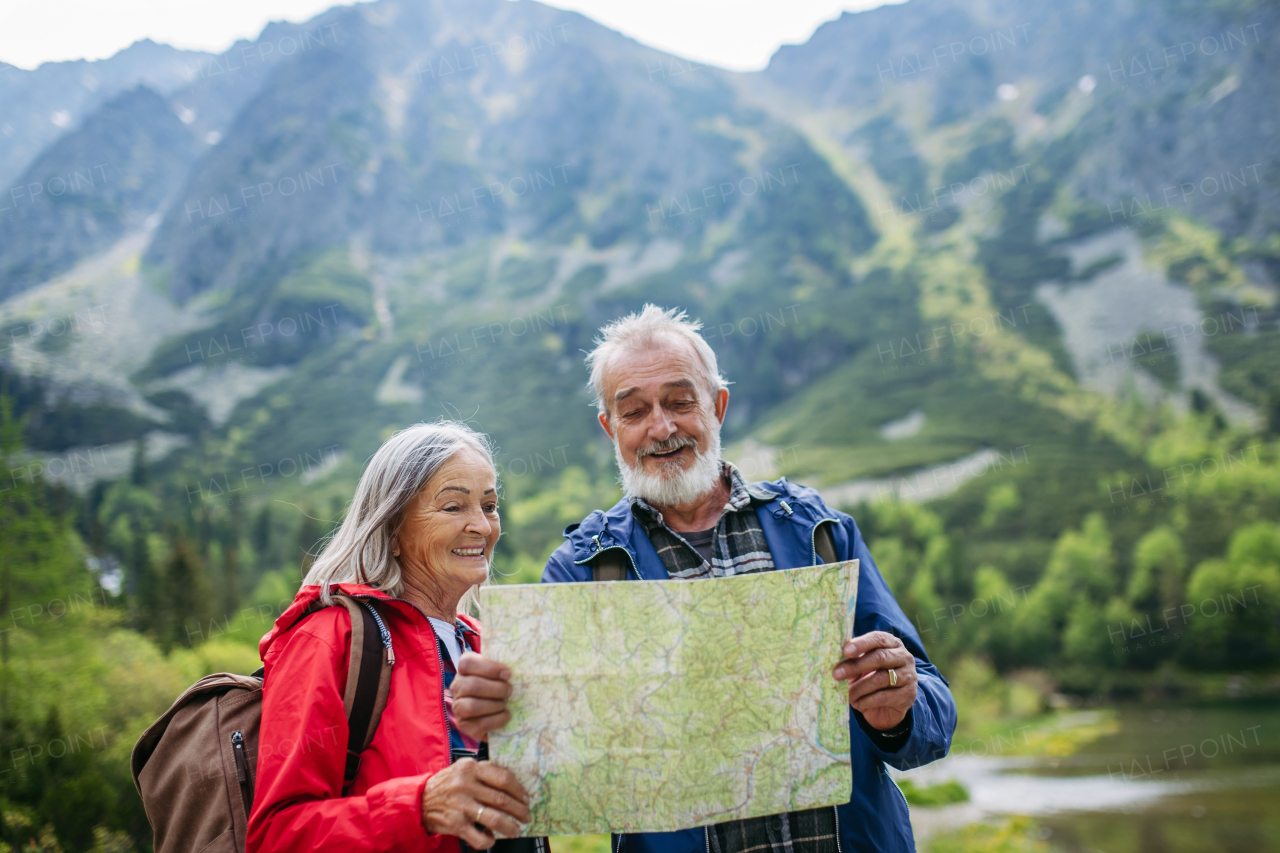 Active elderly couple hiking together in autumn mountains, on senior friendly trail. Senior spouses on the vacation in the mountains celebrating anniversary. Senior tourists with backpacks reading map, preparing for hike.