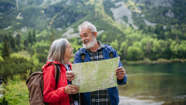 Active elderly couple hiking together in autumn mountains, on senior friendly trail. Senior spouses on the vacation in the mountains celebrating anniversary. Senior tourists with backpacks reading map, preparing for hike.