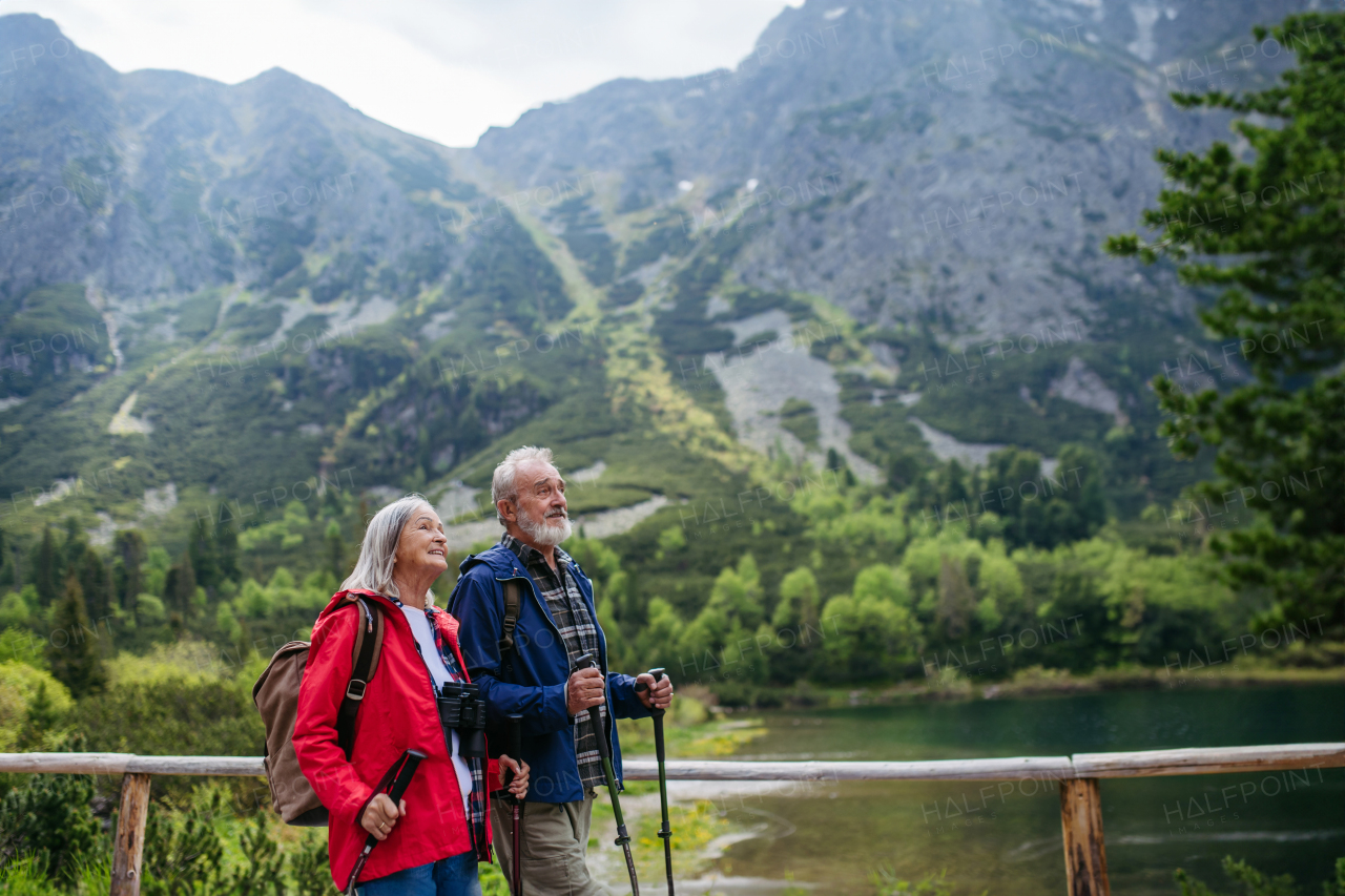 Active elderly couple hiking together in autumn mountains, on senior-friendly trail. Husband and wife walking by lake, enjoying nature. Senior tourists using trekking poles for stability.