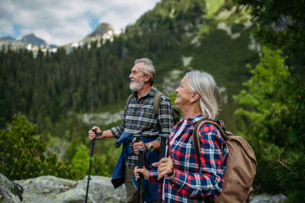 Potrait of active senior woman hiking with husband in autumn mountains, on senior friendly trail. Senior tourist with backpack using trekking poles for stability.