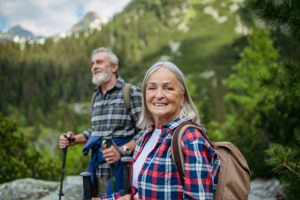 Potrait of active senior woman hiking with husband in autumn mountains. on senior friendly trail. Senior tourist with backpack using trekking poles for stability.