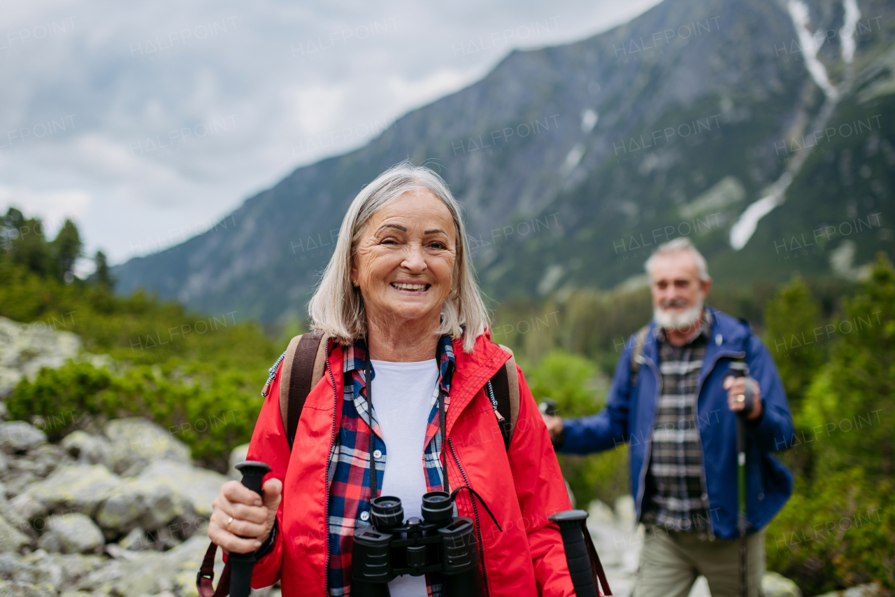 Potrait of active senior woman hiking with husband in autumn mountains. on senior friendly trail. Senior tourist with backpack using trekking poles for stability.