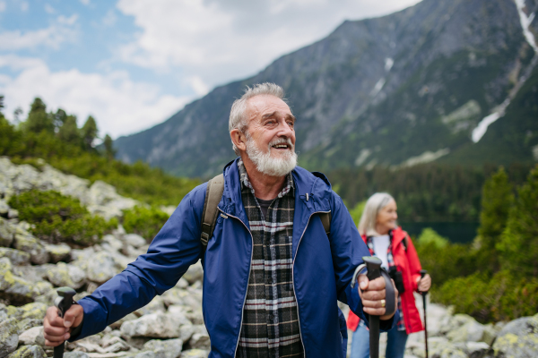 Potrait of active senior man hiking with wife in autumn mountains. on senior friendly trail. Senior tourist with backpack using trekking poles for stability.