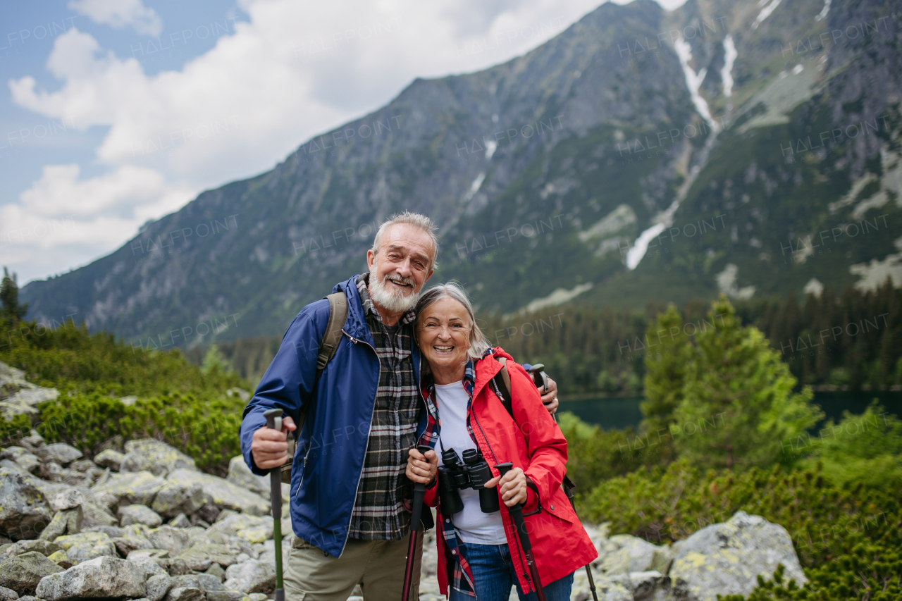 Active elderly couple hiking together in autumn mountains, on senior friendly trail. Senior spouses on the vacation in the mountains celebrating anniversary. Senior tourist with backpacks using trekking poles for stability.