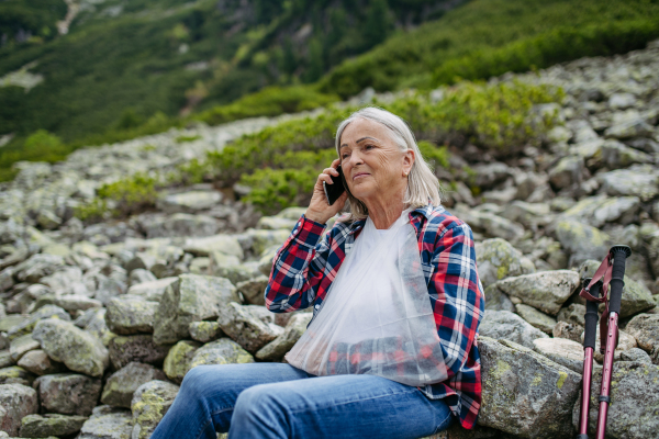 Senior woman calling mountain rescue for herself. A senior woman injured her arm during hike in the mountains. Tourist went off-trail and fell.