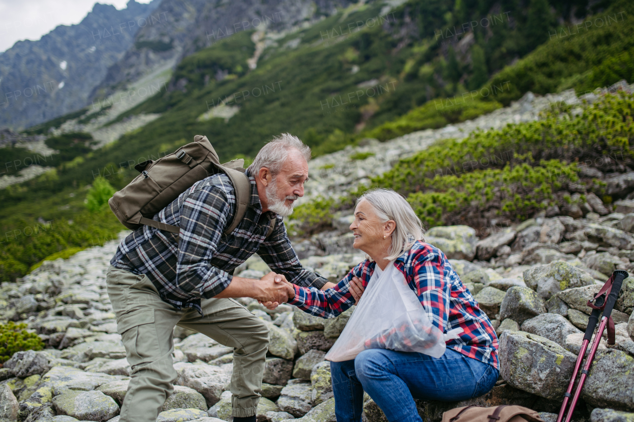 Senior man helping injured female tourist. A senior woman injured her arm during hike in the mountains. Tourist went off-trail and fell.