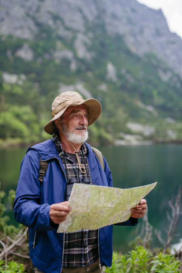 Potrait of active senior man hiking in autumn mountains, on senior friendly trail. Senior tourist with backpack looking for his trekking trail on paper map,