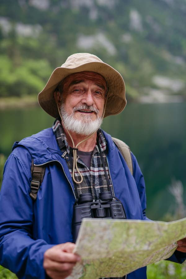 Potrait of active senior man hiking in autumn mountains, on senior friendly trail. Senior tourist with backpack looking for his trekking trail on paper map,