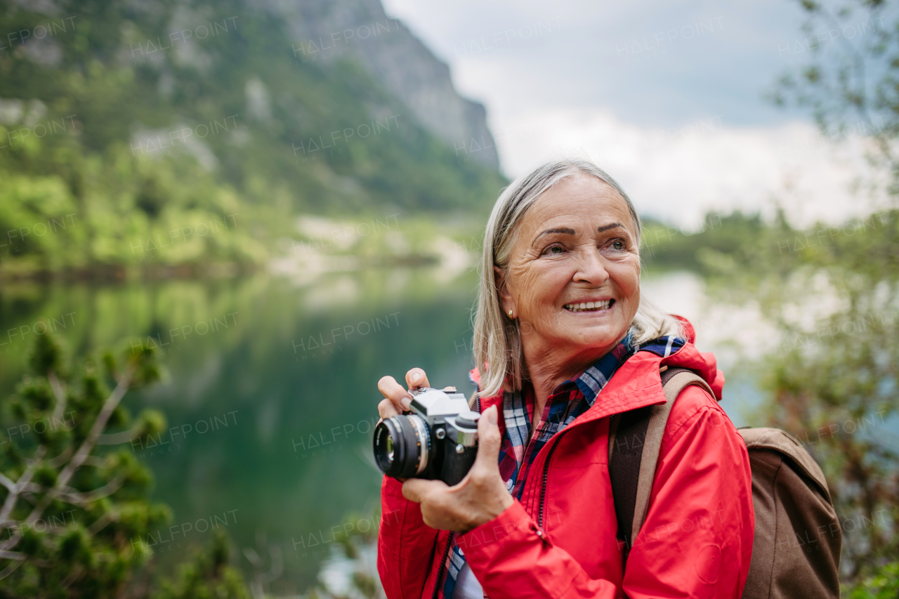 Potrait of active senior woman hiking in autumn mountains, on senior friendly trail. Senior tourist with backpack taking pictures with analog camera.