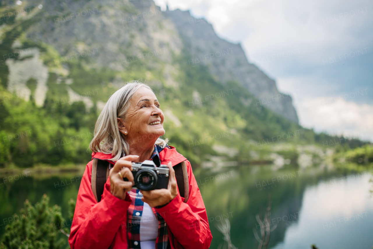 Potrait of active senior woman hiking in autumn mountains, on senior friendly trail. Senior tourist with backpack taking pictures with analog camera.