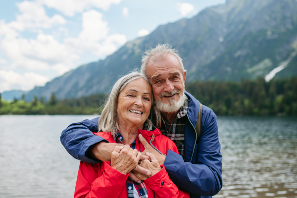 Portrait of beautiful active elderly couple hiking together in autumn mountains. Senior spouses on the vacation in the mountains celebrating anniversary. Senior tourists embrancing each other in front of lake.