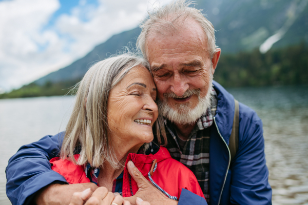 Portrait of beautiful active elderly couple hiking together in autumn mountains. Senior spouses on the vacation in the mountains celebrating anniversary. Senior tourists embrancing each other in front of lake.