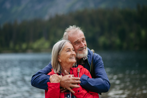 Portrait of beautiful active elderly couple hiking together in autumn mountains,. Senior spouses on the vacation in the mountains celebrating anniversary. Senior tourists embrancing each other in front of lake.