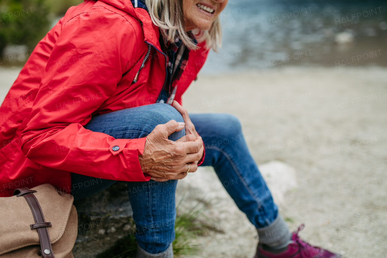 Senior woman injured leg during hike in the mountains. Tourist went off-trail and fell. Elderly tourist feeling pain under kneecap, also known as Hiker's knee.