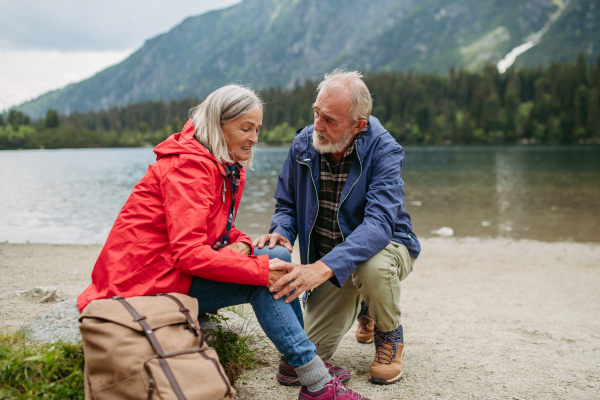 Senior woman injured leg during hike in the mountains. Tourist went off-trail and fell. Elderly tourist resting on the ground, feeling pain under her kneecap, also known as Hiker's knee.