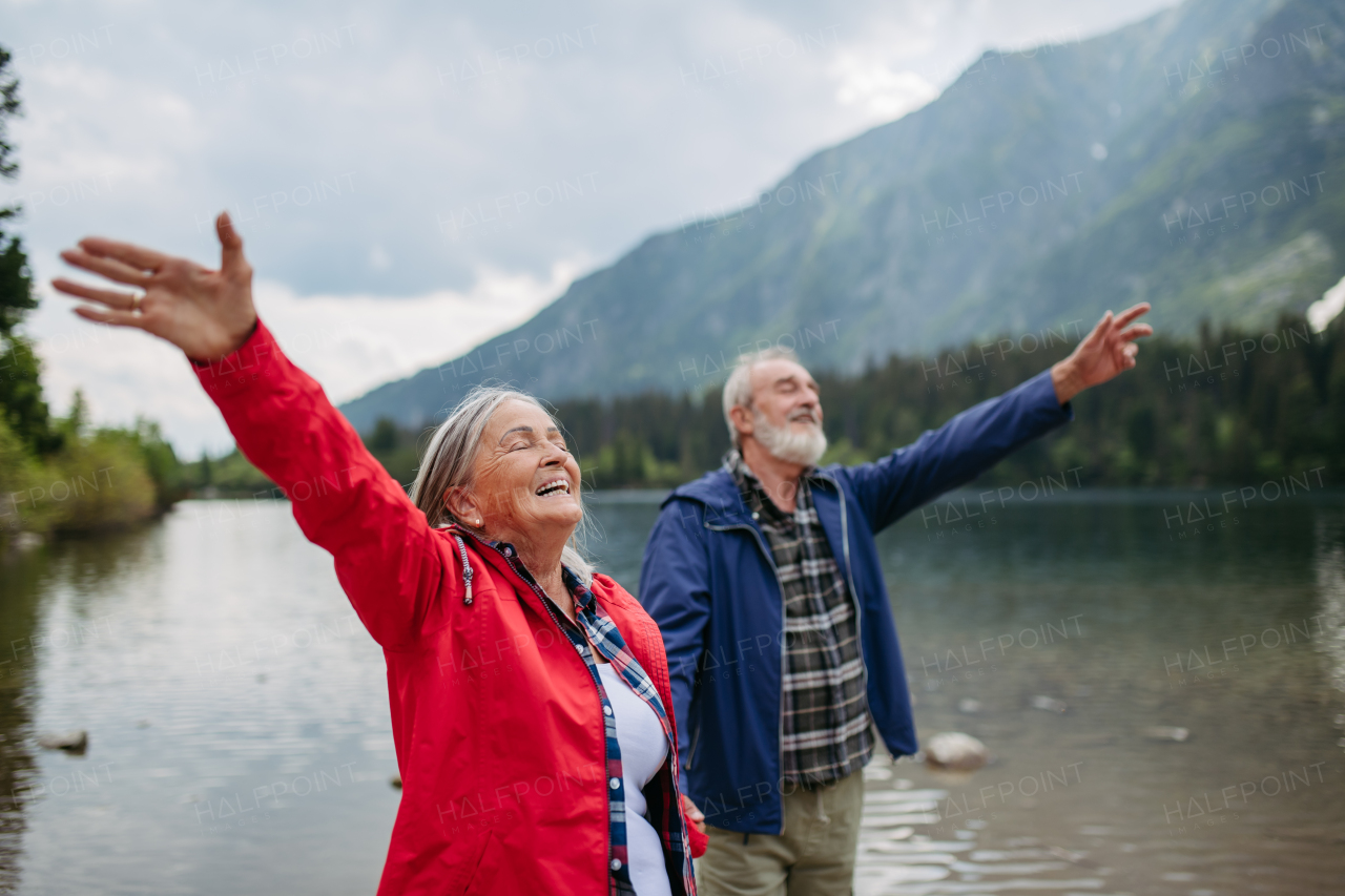 Waist up shot of happy elderly couple with hands in the air. Senior husband and wife feeling satisfied after hike in autumn mountains.