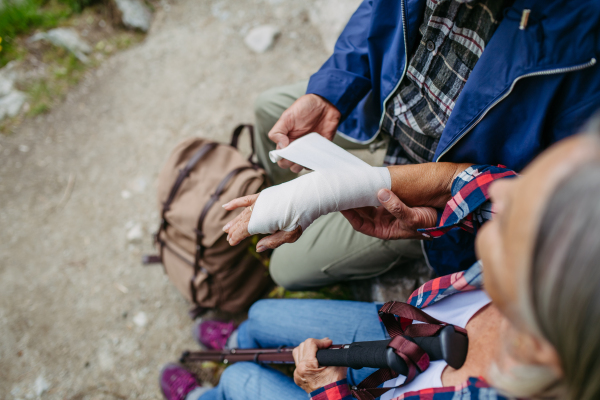 Senior man helping injured female tourist. A senior woman injured her arm during hike in the mountains. Tourist went off-trail and fell.