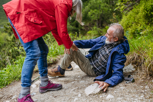 Senior man injured his leg during hike in the mountains. Tourist went off-trail and fell. Elderly tourist resting on the ground, feeling pain under his kneecap, also known as Hiker's knee.