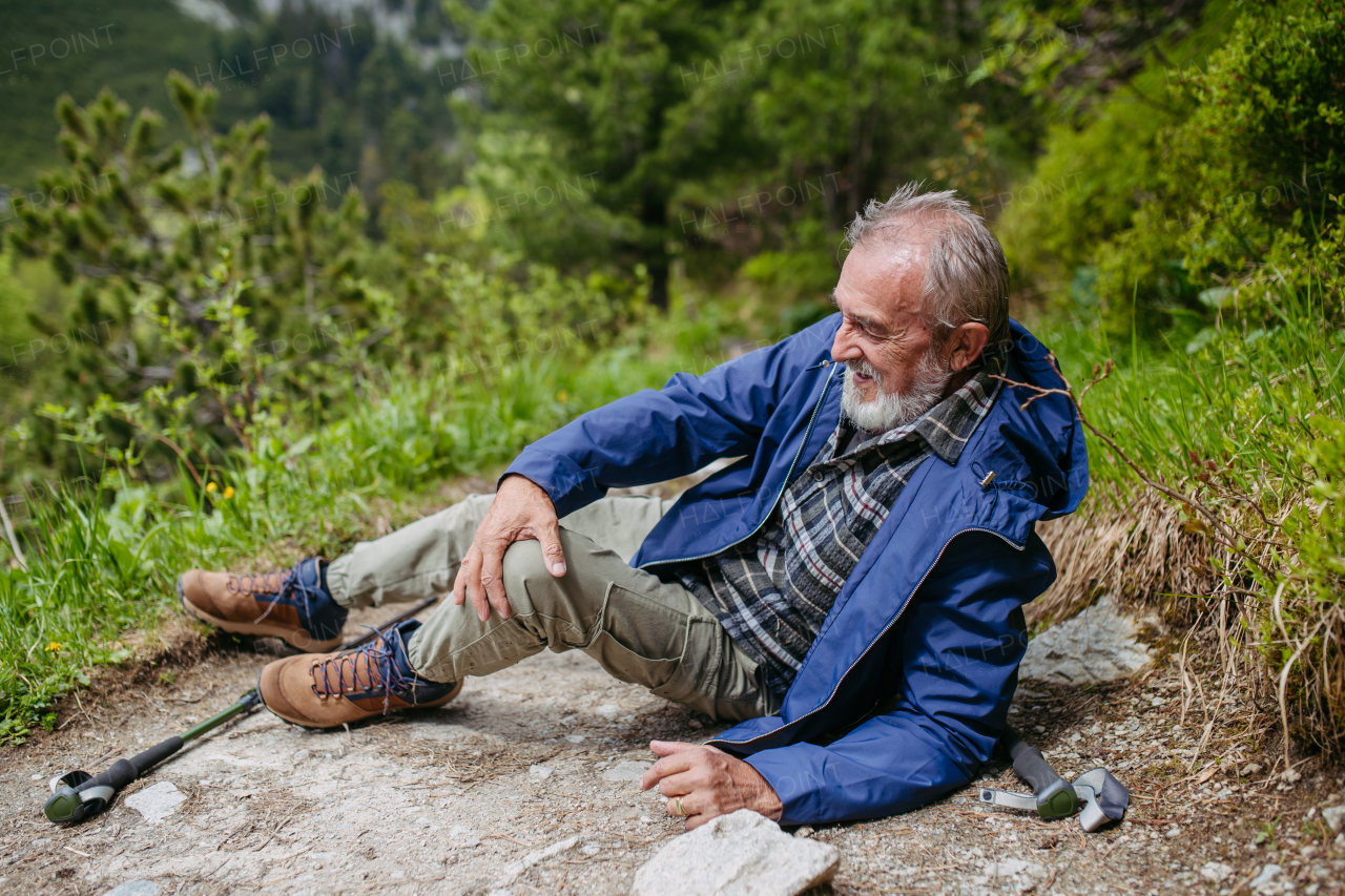 Senior man injured his leg during hike in the mountains. Tourist went off-trail and fell. Elderly tourist resting on the ground, feeling pain under his kneecap, also known as Hiker's knee.