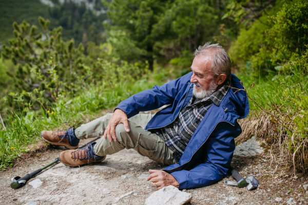 Senior man injured his leg during hike in the mountains. Tourist went off-trail and fell. Elderly tourist resting on the ground, feeling pain under his kneecap, also known as Hiker's knee.