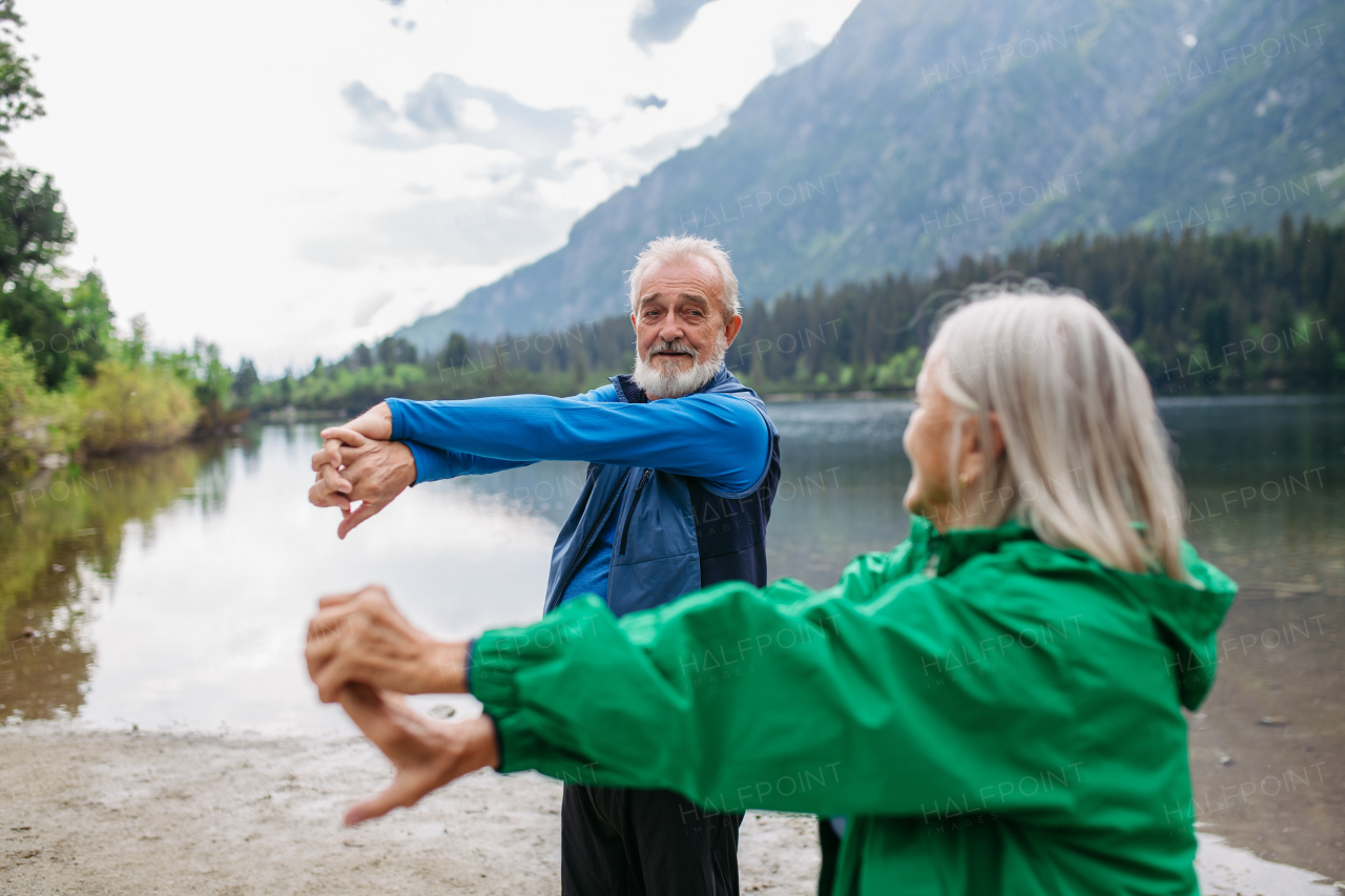 Senior couple doing outdoor yoga, tai chi, pilates by the lake in the autumn. Elderly husband and wife spending active vacation in the mountains, enjoying combination of physical activity and relaxation. Pensioners stretching after outdoor workout