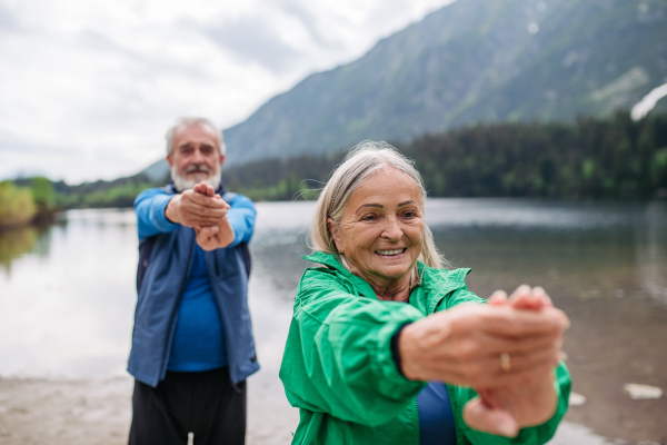 Senior couple doing outdoor yoga, tai chi, pilates by the lake in the autumn. Elderly husband and wife spending active vacation in the mountains, enjoying combination of physical activity and relaxation. Pensioners stretching after outdoor workout