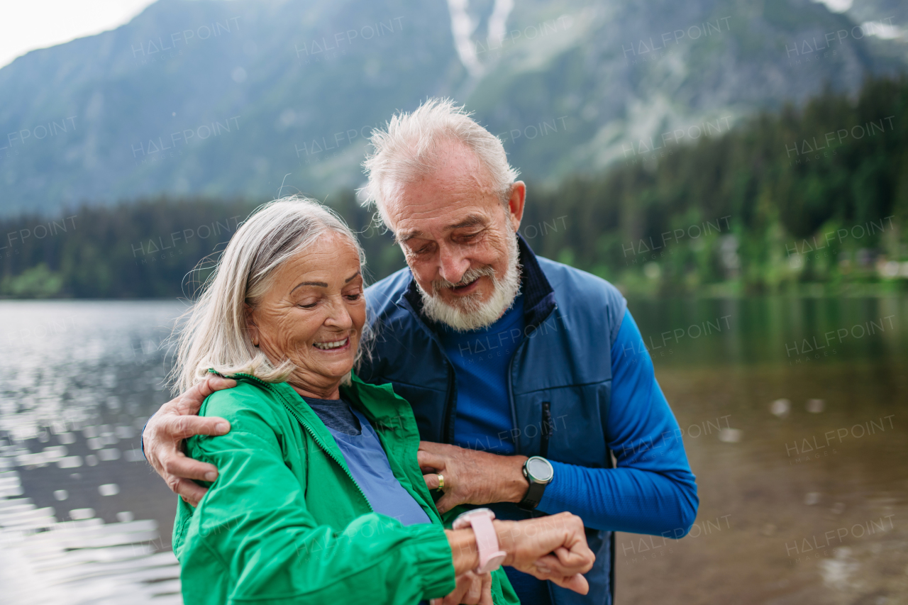 Senior woman checking her vital functions, heart rate, on smartwatch after hike. Senior tourists looking at smartwatch, tracking their speed, pace, distance and performance, using app.