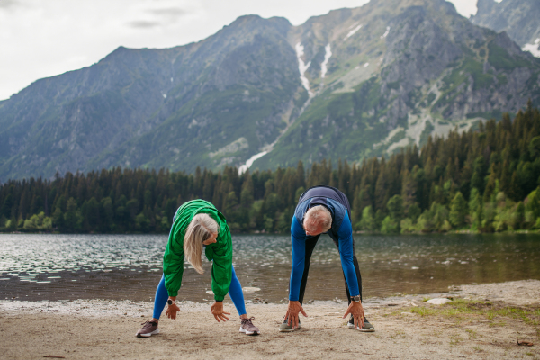 Senior couple doing outdoor yoga, tai chi, pilates by the lake in the autumn. Elderly husband and wife spending active vacation in the mountains, enjoying combination of physical activity and relaxation. Pensioners stretching after outdoor workout