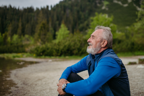 Potrait of active senior man resting after hiking in autumn mountains. Thoughtful elderly man enjoying view of untouched nature.