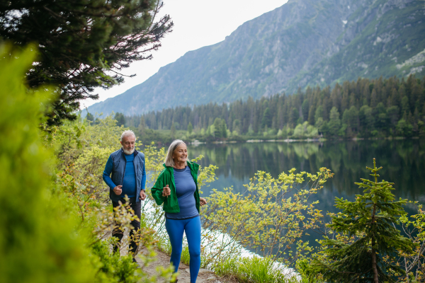 Senior couple running by the lake in the autumn. Elderly husband and wife spending active vacation in the mountains, enjoying combination of physical activity and relaxation.