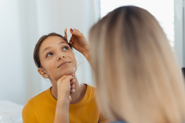 Pediatrician putting eye drops into girls eyes. Ophthalmologist treating an eye infection, allergy, or inflammation using prescribed eye drops.