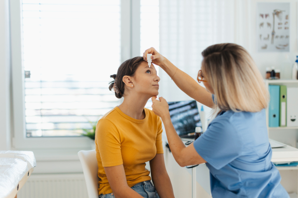 Pediatrician putting eye drops into girls eyes. Ophthalmologist treating an eye infection, allergy, or inflammation using prescribed eye drops.