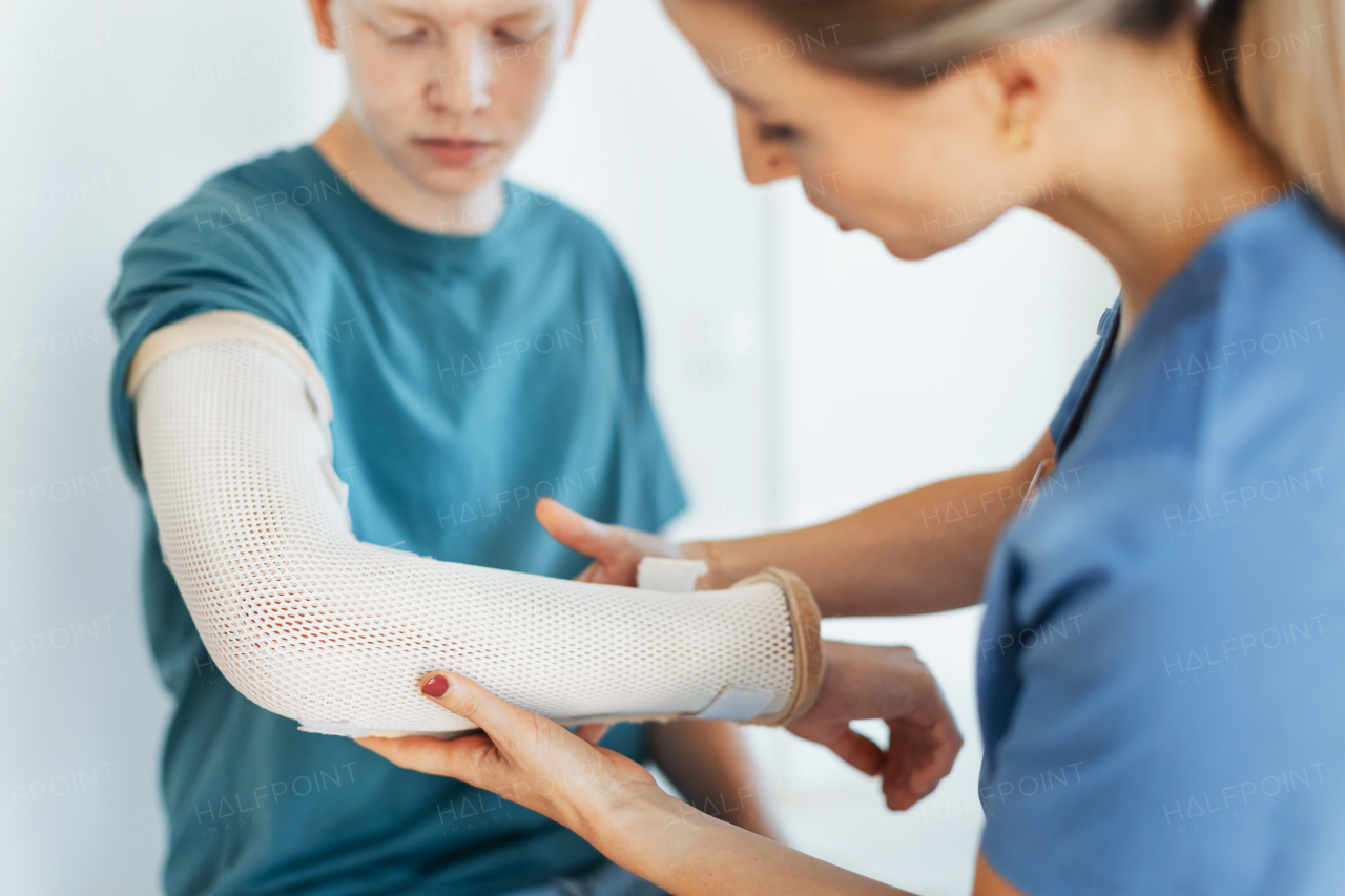 Doctor checking orthopedic cast, brace on a teenage patient's broken arm. Teenage boy is healing a fracture after an accident.