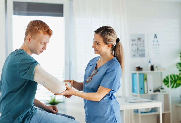 Doctor checking orthopedic cast, brace on a teenage patient's broken arm. Teenage boy is healing a fracture after an accident.