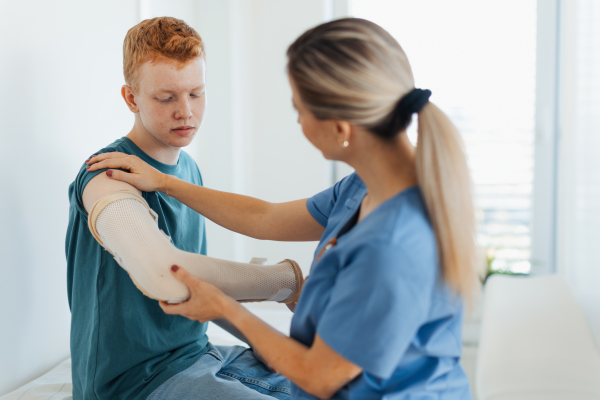 Doctor checking orthopedic cast, brace on a teenage patient's broken arm. Teenage boy is healing a fracture after an accident.