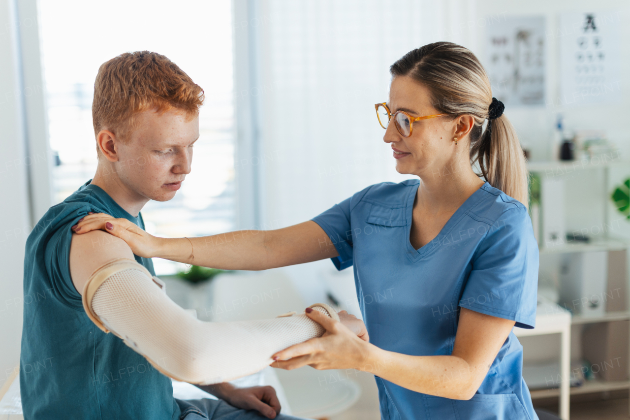 Doctor checking orthopedic cast, brace on a teenage patient's broken arm. Teenage boy is healing a fracture after an accident.