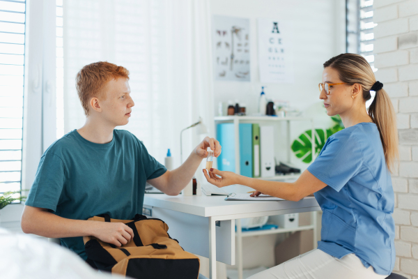 Diabetologist doctor doing regular urine test for the teenage diabetic patient in diabetes clinic. Examining a urine sample to detect glucose, kidneys function, ketones or infections.