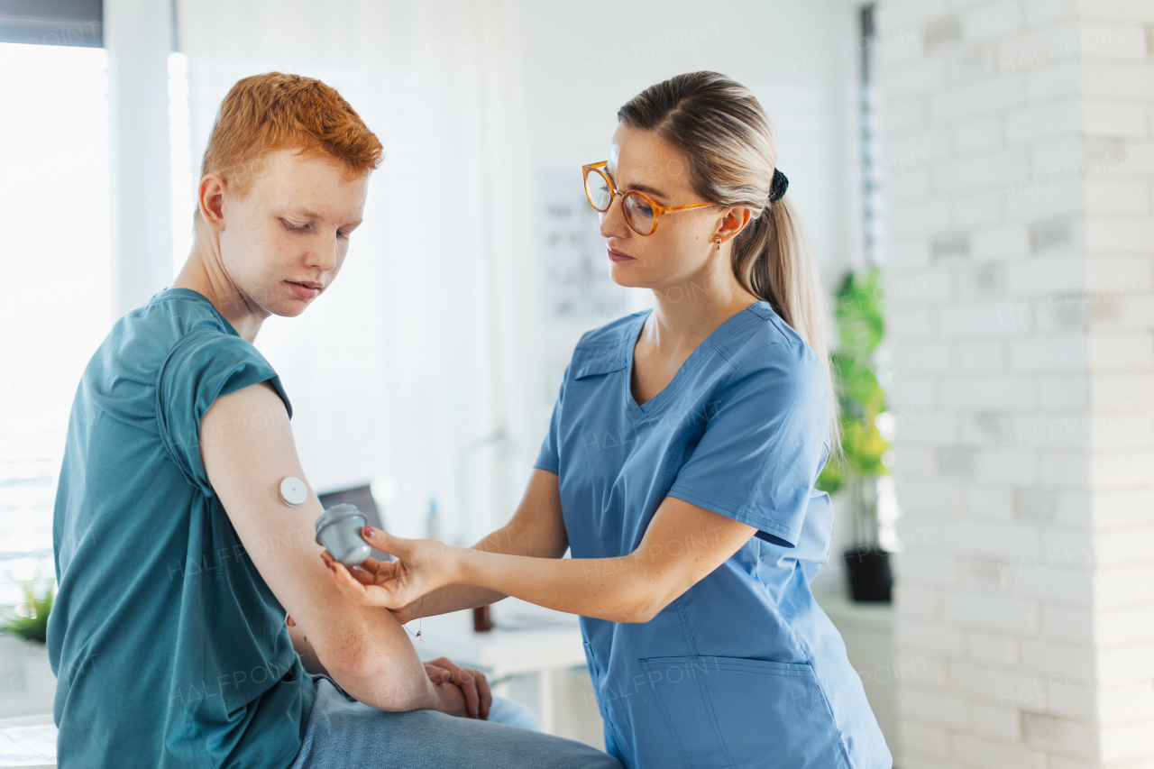 Diabetologist doctor connecting continuous glucose monitor sensor to smartphone, checking teenage boy's glucose data in the real time. Endocrinologist taking care of teenage diabetic patient.