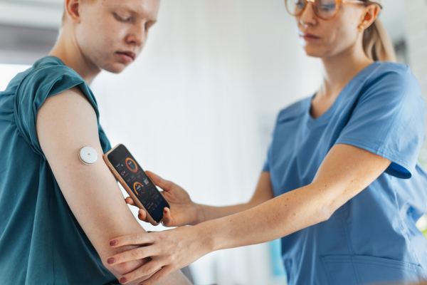 Diabetologist doctor connecting continuous glucose monitor sensor to smartphone, checking teenage boy's glucose data in the real time. Endocrinologist taking care of teenage diabetic patient.