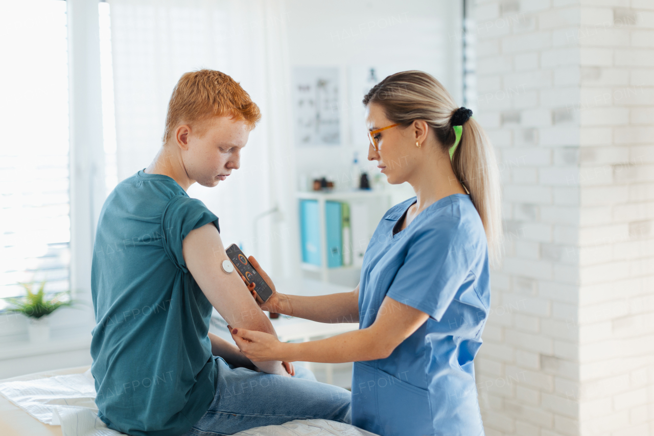 Diabetologist doctor connecting continuous glucose monitor sensor to smartphone, checking teenage boy's glucose data in the real time. Endocrinologist taking care of teenage diabetic patient.