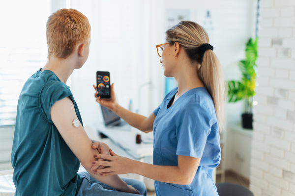 Diabetologist doctor teaching young patient ho to connect continuous glucose monitor sensor to his smartphone. Doctor checking teenage boy's glucose data in the real time. Endocrinologist taking care of teenage diabetic patient.