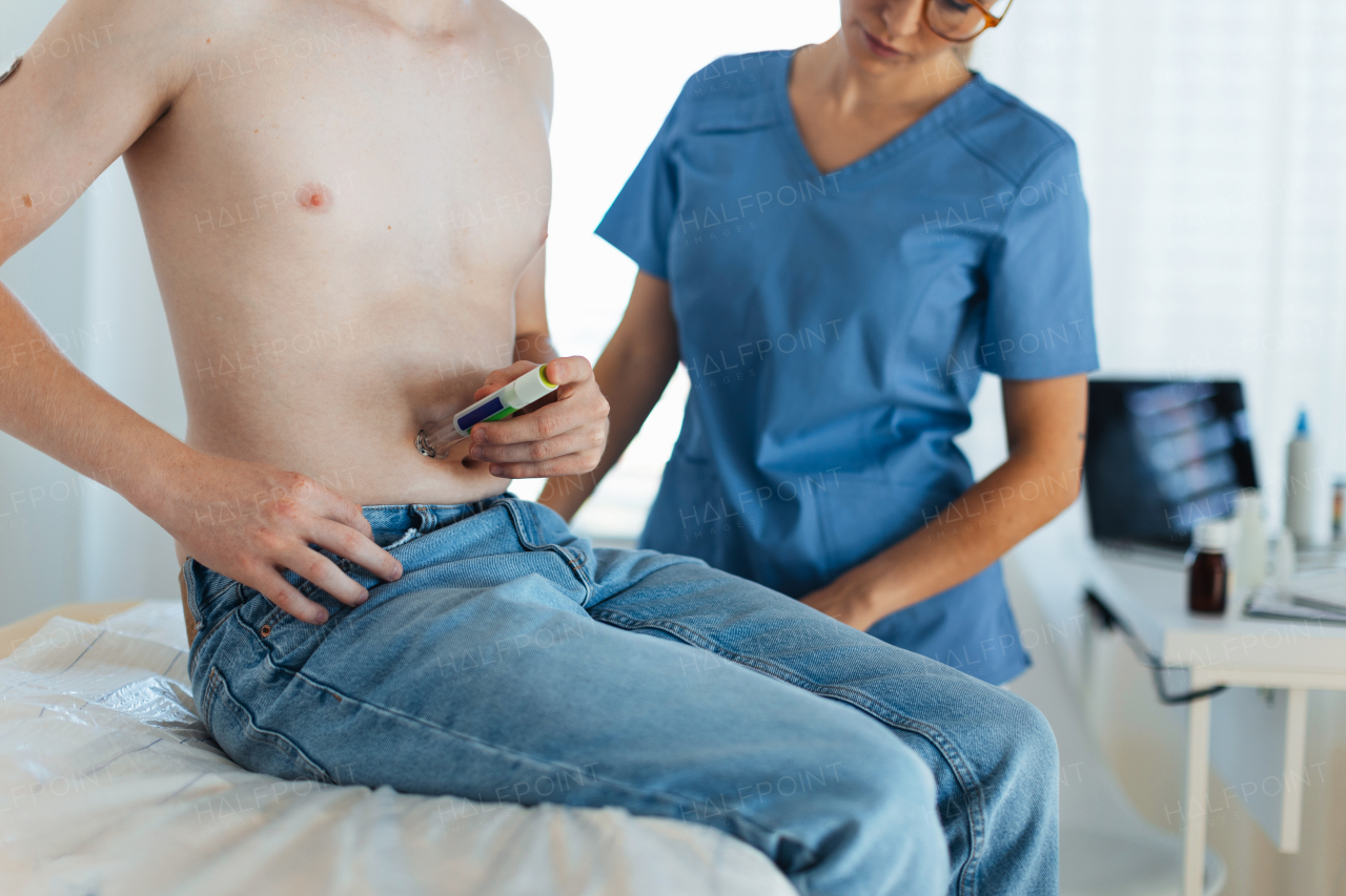 Diabetologist doctor teaching teenage patient how to inject insulin into abdomen, using insulin pen. Endocrinologist injecting medicine into boy's abdomen.