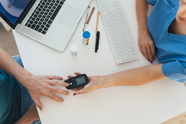 Diabetologist doctor testing blood sample on glucometer in diabetes clinic. Doctor taking blood sample from boy's finger. Paediatric diabetes in teenage boy, young man.