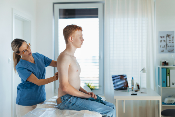 Female doctor examining teenage boy's skin, checking acne and moles. Skin cancer screening. Boy visiting dermatologist for annual preventive skin exam. Concept of preventive health care for adolescents.