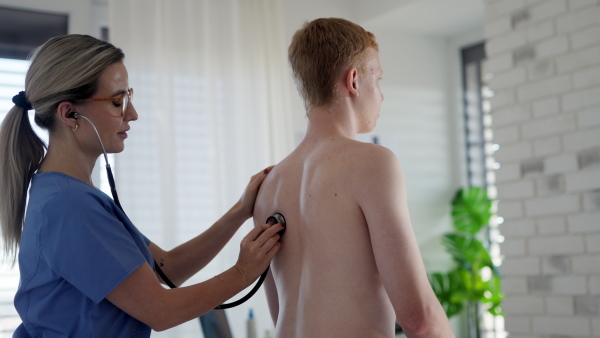 Female doctor examining teenage boy's skin. Boy visiting doctor for annual preventive exam. Concept of preventive health care for adolescents.